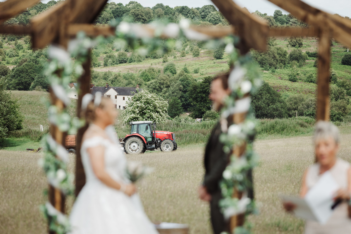 Massey Ferguson in focus whilst bride and groom are out of focus at farm ceremony