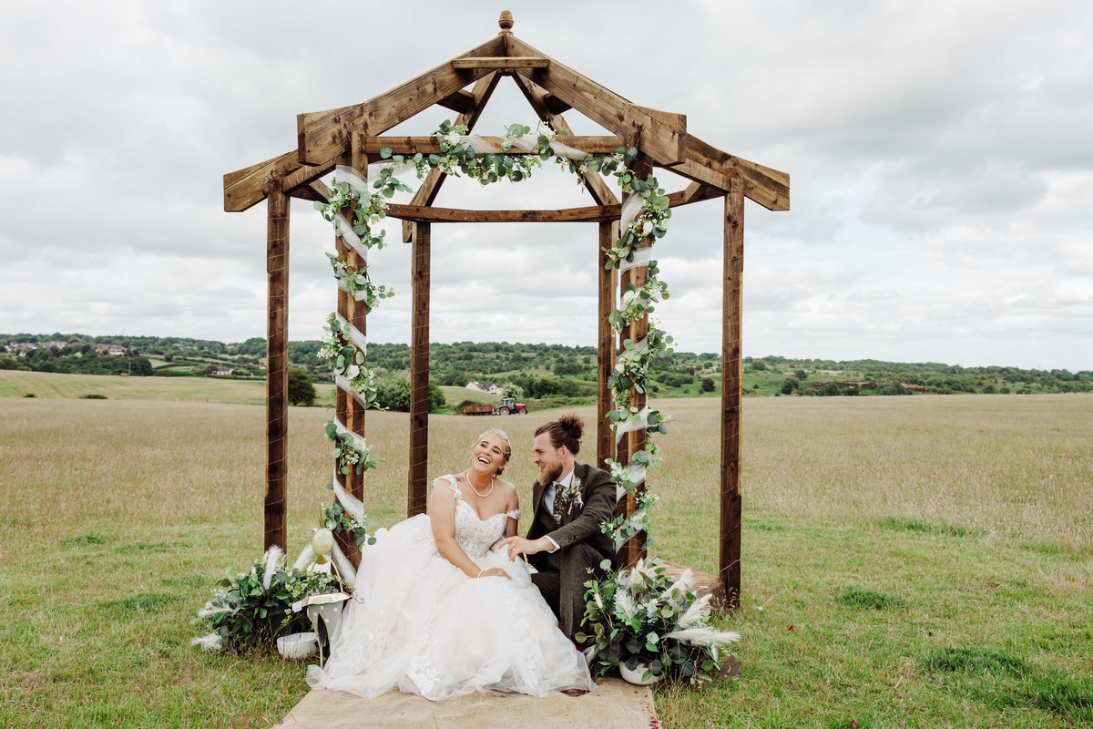 Bride and Groom sit on wooden arch where they said their vows on a Staffordshire farm