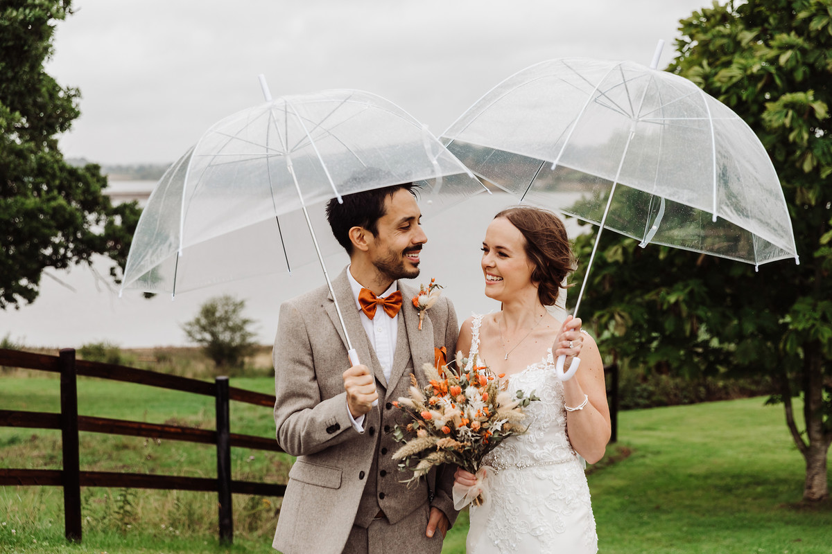 Bride and groom portraits under clear umbrellas at Blithfield Lakeside Barns