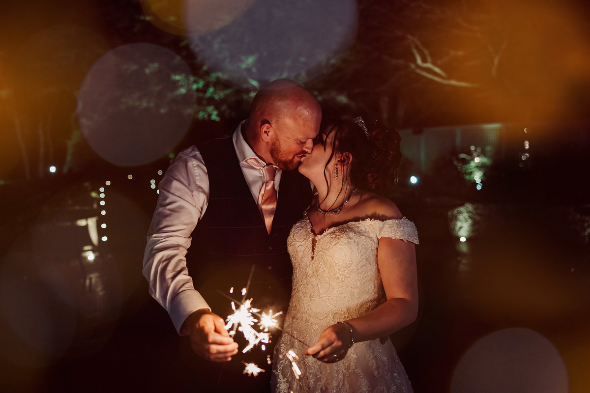 Bride and groom kiss with sparklers at their winter wedding at moddershall oaks
