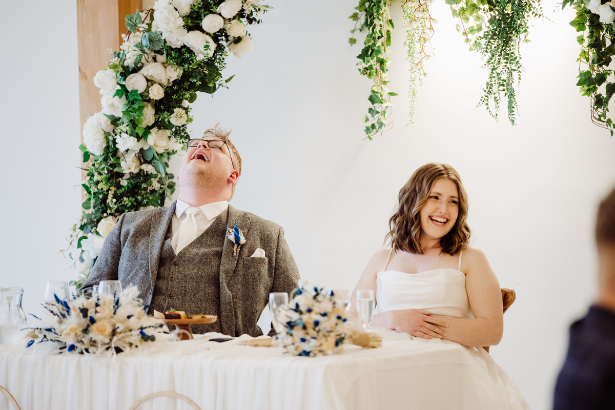 Bride and groom laugh during speeches at Hanbury wedding barn