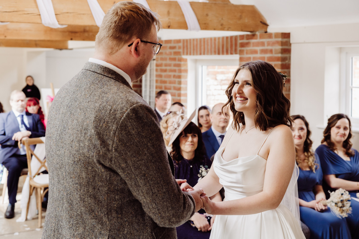 Bride smiles at the groom during the ceremony at Hanbury wedding barns