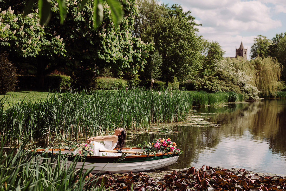 Bride throws head back in a rowing boat on the lake at The Moat House