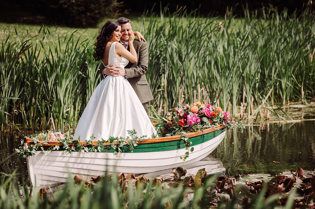 Bride and groom stand in the rowing boat at The Moat House in Acton Trussell