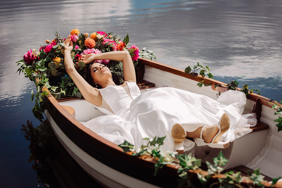 Bride lies in a rowing boat in the sunshine at The Moat House