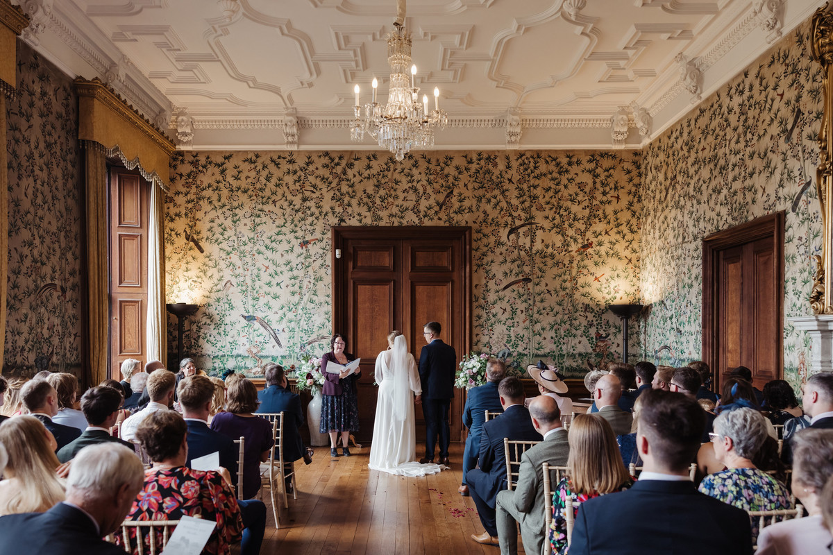 A bride and groom hold hands during the ceremony in the drawing room at Sandon Hall