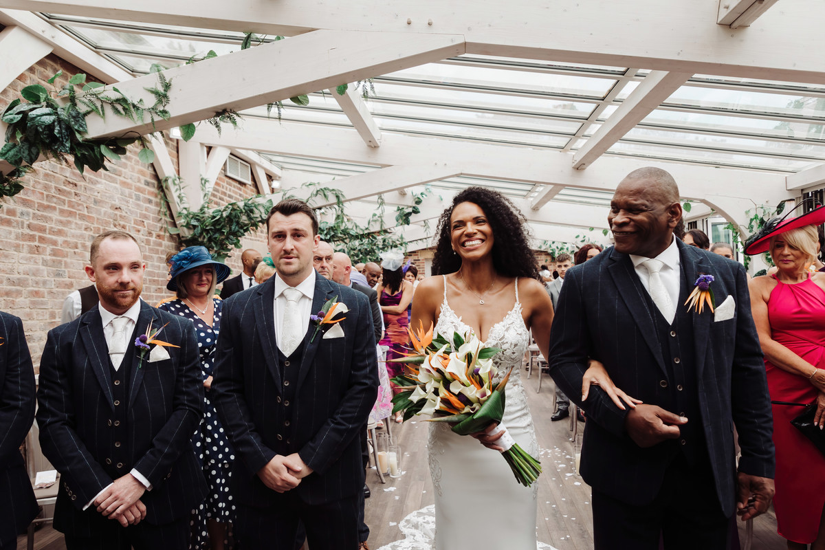 Huge smiles from a happy bride and dad as they walk down the aisle at Foxtail Barns