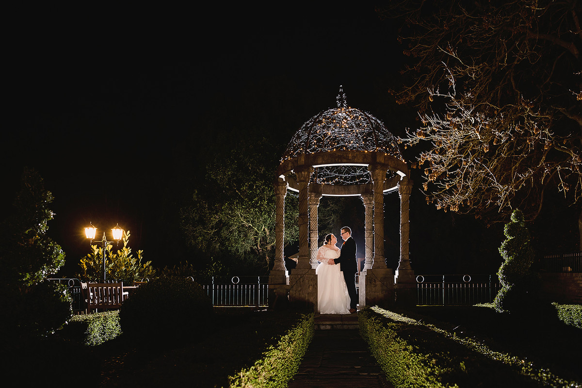 Bride and groom beneath fairy lights for a night time wedding portrait