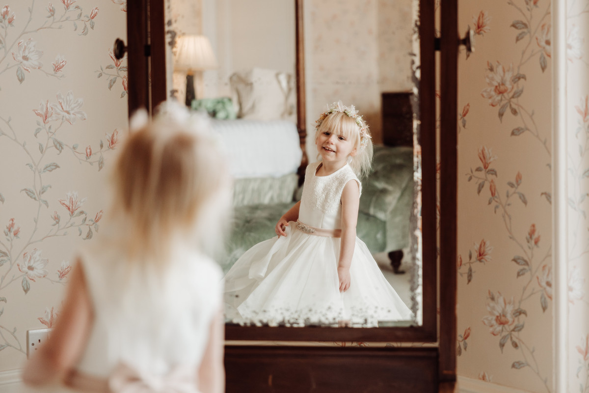 Flower girl admires herself in the mirror at Sandon Hall