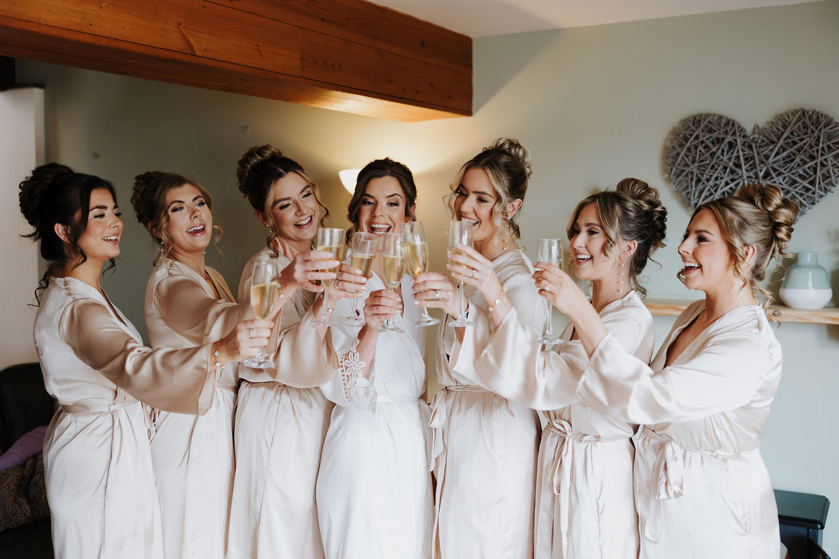 Bridal party raise a glass in matching robes at Blithfield Lakeside Barns
