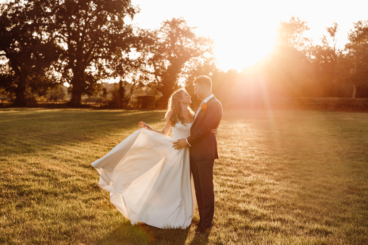 Bride and Groom embrace in a field at sunset