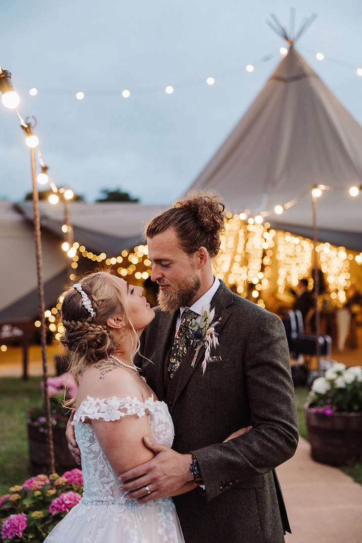 Bride and groom outside tipi lit with fairylights on their wedding day in Staffordshire