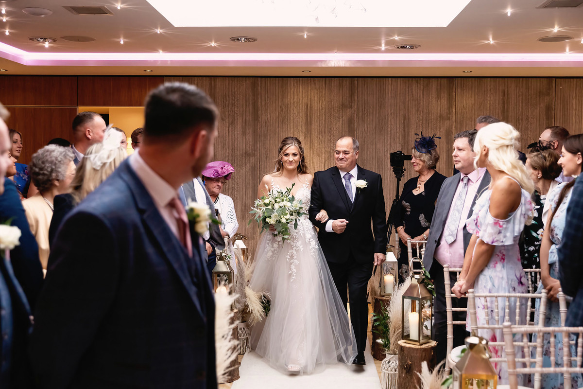 Bride walks down the aisle with dad during indoor ceremony at Moddershall Oaks